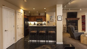 A modern kitchen with a central island, bar stools, a refrigerator, and a microwave.