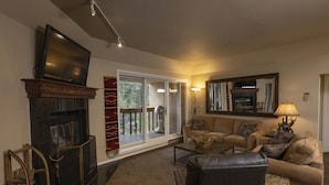 A living room with a fireplace, a sofa set, a television, and a large window with a view of the outdoors.