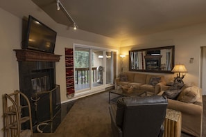 A living room with a fireplace, a sofa set, a television, and a large window with a view of the outdoors. - Village Center 511 - Managed by Purgatory Resort (Durango)