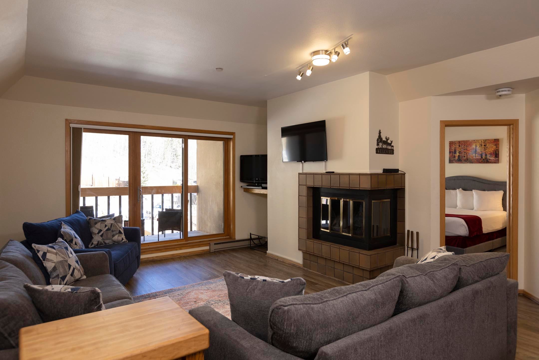 A living room with a sofa, a TV, a fireplace, and a sliding glass door.