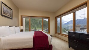 A bedroom with a large bed, a dresser, and a view of mountains through large windows. - Village Center 612 - Managed by Purgatory Resort (Durango)