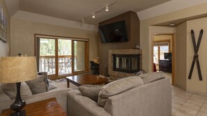 A living room with a fireplace, a sofa, a coffee table, and a TV mounted on the wall. - Village Center 612 - Managed by Purgatory Resort (Durango)