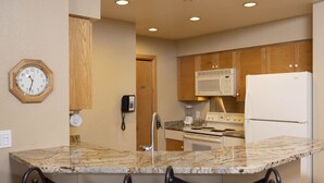 A kitchen with granite countertops, a stove, microwave, and refrigerator. There is a clock on the wall and a phone on the wall. - Village Center 612 - Managed by Purgatory Resort (Durango)