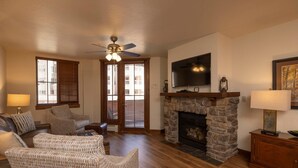 A spacious living room with a stone fireplace, comfortable seating, a ceiling fan, and a flat-screen TV mounted above the fireplace. - Purgatory Lodge 104 - Managed by Purgatory Resort (Durango)