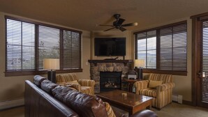 A living room with a fireplace, leather sofa, striped armchairs, and a ceiling fan. - Purgatory Lodge 201 - Managed by Purgatory 201 (Durango)