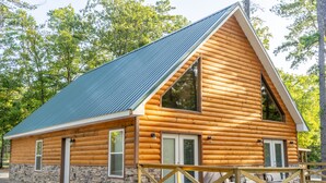 A log cabin with a stone foundation, large windows, and a covered porch. - Cabin C at Safe Harbor Brady Mountain on Lake Ouachita! (Royal)