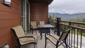 Un balcón con mesa y sillas, una puerta corredera de vidrio y vistas a las montañas.