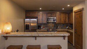 A kitchen with wooden cabinets, stainless steel appliances, a granite countertop, and a bar area with stools. - Purgatory Lodge 204 - Managed by Purgatory Resort (Durango)