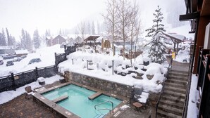 A swimming pool with a stone wall and a wooden deck, surrounded by snow-covered ground and trees.
