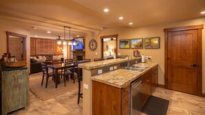 A spacious kitchen with a granite countertop, wooden cabinets, and a built-in dishwasher. There is a dining area with a wooden table and chairs, and a cozy living room with a sofa and a fireplace.
