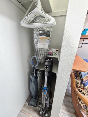 Enjoy a functional space with a wall-mounted ironing board, vacuum cleaner, and comfortable chair.