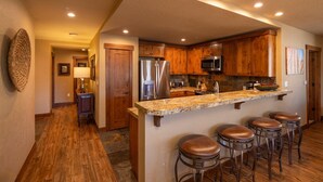 A kitchen with wooden cabinets, a granite countertop, stainless steel appliances, and bar stools. - Purgatory Lodge 402 - Managed by Purgatory Resort (Durango)