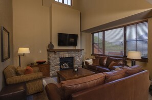 A living room with a stone fireplace, leather sofas, and a flat-screen TV mounted above it.