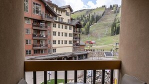 A balcony with two chairs and a table, overlooking a ski resort with buildings and a mountain. - Cozy Studio for 2 at Purgatory Village - Kendall 335, Durango, CO with Plaza View. (Durango)