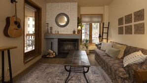A living room with a fireplace, a sofa, a coffee table, a guitar, and a patterned rug. - Cozy Studio for 2 at Purgatory Village - Kendall 335, Durango, CO with Plaza View. (Durango)