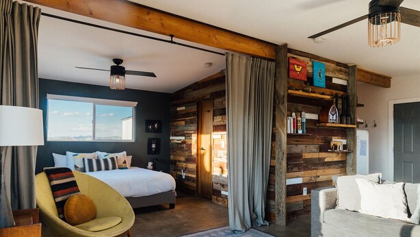 A modern bedroom with a large bed, a chair, a sofa, and a wooden wall. - Secluded Retreat-Hot Tub, Fire Pit, Outdoor Shower (Joshua Tree)