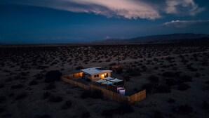 A remote desert location with a single house featuring a fenced yard and a small patio area. - Secluded Retreat-Hot Tub, Fire Pit, Outdoor Shower (Joshua Tree)