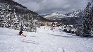 Une piste de ski enneigée, avec un chalet visible au loin.