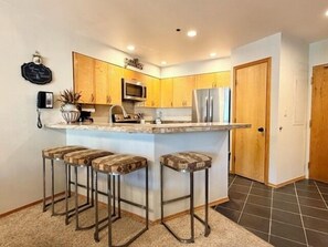 A kitchen with wooden cabinets, stainless steel appliances, and a bar stool seating area. - Kendall 236 - Managed by Purgatory Resort (Durango)