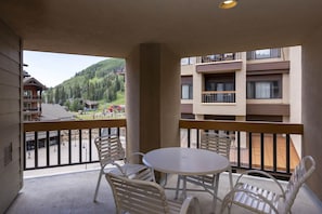 Ein Balkon mit Tisch und Stühlen, mit Blick auf einen Skigebiet mit Gebäuden und einem bewaldeten Hügel.
