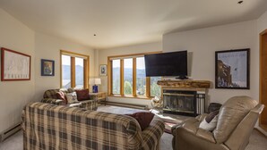 A living room with a fireplace, a television, and a large window with a mountain view. - Kendall 437 - Managed by Purgatory Resort (Durango)