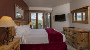 A bedroom with a bed, a wooden dresser, a TV, and a window with a view of greenery. - Kendall 437 - Managed by Purgatory Resort (Durango)