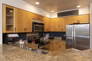 Una cocina moderna con encimeras de granito, electrodomésticos de acero inoxidable, armarios de madera y un microondas integrado.