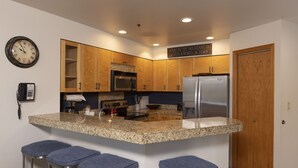 A kitchen with granite countertops, wooden cabinets, a stainless steel refrigerator, and a clock on the wall. - Kendall 437 - Managed by Purgatory Resort (Durango)