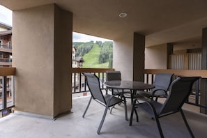 Un balcón con una mesa redonda y cuatro sillas, con vistas a un paisaje montañoso que incluye un telesilla.
