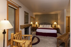 A bedroom with a bed, two bedside tables with lamps, a wooden chair, a fireplace, and a large mirror.