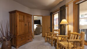 A room with a wooden cabinet, a wooden chair, a lamp, and a view through a window. - Kendall 437 - Managed by Purgatory Resort (Durango)