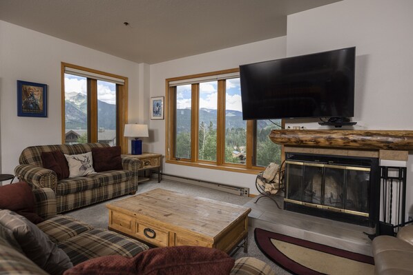 A living room with a fireplace, a television, and large windows with a mountain view.