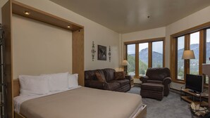 A bedroom with a large bed, a leather armchair, a sofa, and a TV. There are windows with a mountain view. - Studio in Purgatory Village with mountain views, pool, hot tub. (Durango)