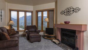 A cozy living room with a fireplace, leather furniture, and large windows offering mountain views. - Studio in Purgatory Village with mountain views, pool, hot tub. (Durango)