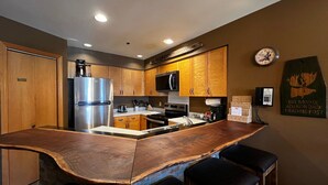 A kitchen with wooden cabinets, stainless steel appliances, a bar area with stools, and a clock on the wall. - Kendall 540 - Managed by Purgatory Resort (Durango)