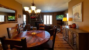 A dining area with a round wooden table, chairs, a chandelier, and a television displaying a sports game. - Kendall 540 - Managed by Purgatory Resort (Durango)