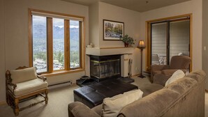 Un salon doté d’une cheminée, de grandes fenêtres, d’une vue sur les montagnes et d’un coin salon confortable.
