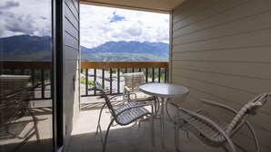 Un balcon avec une table et des chaises, offrant une vue sur les montagnes et un parking.