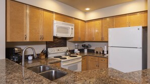 Une cuisine avec des meubles en bois, une cuisinière blanche, un four à micro-ondes, un réfrigérateur, des comptoirs en granit et des éviers en acier inoxydable.