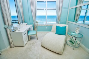 Une chambre avec vue sur l’océan, un bureau avec une lampe, une chaise et une petite table sur laquelle se trouve un livre.