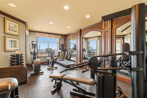 A gym with various exercise equipment, large mirrors, and a window providing a view outside.