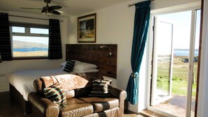 Een slaapkamer met een bed, hoofdeinde, een raam met uitzicht op de omgeving, een plafondventilator en een deur die leidt naar een balkon.