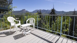 Un balcon avec deux chaises blanches et une table, donnant sur un paysage montagneux.