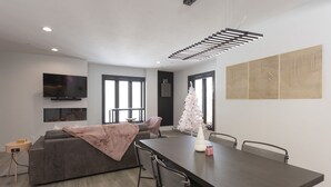 Una sala de estar moderna con una mesa de comedor de madera oscura, un sofá gris y un árbol de Navidad blanco.