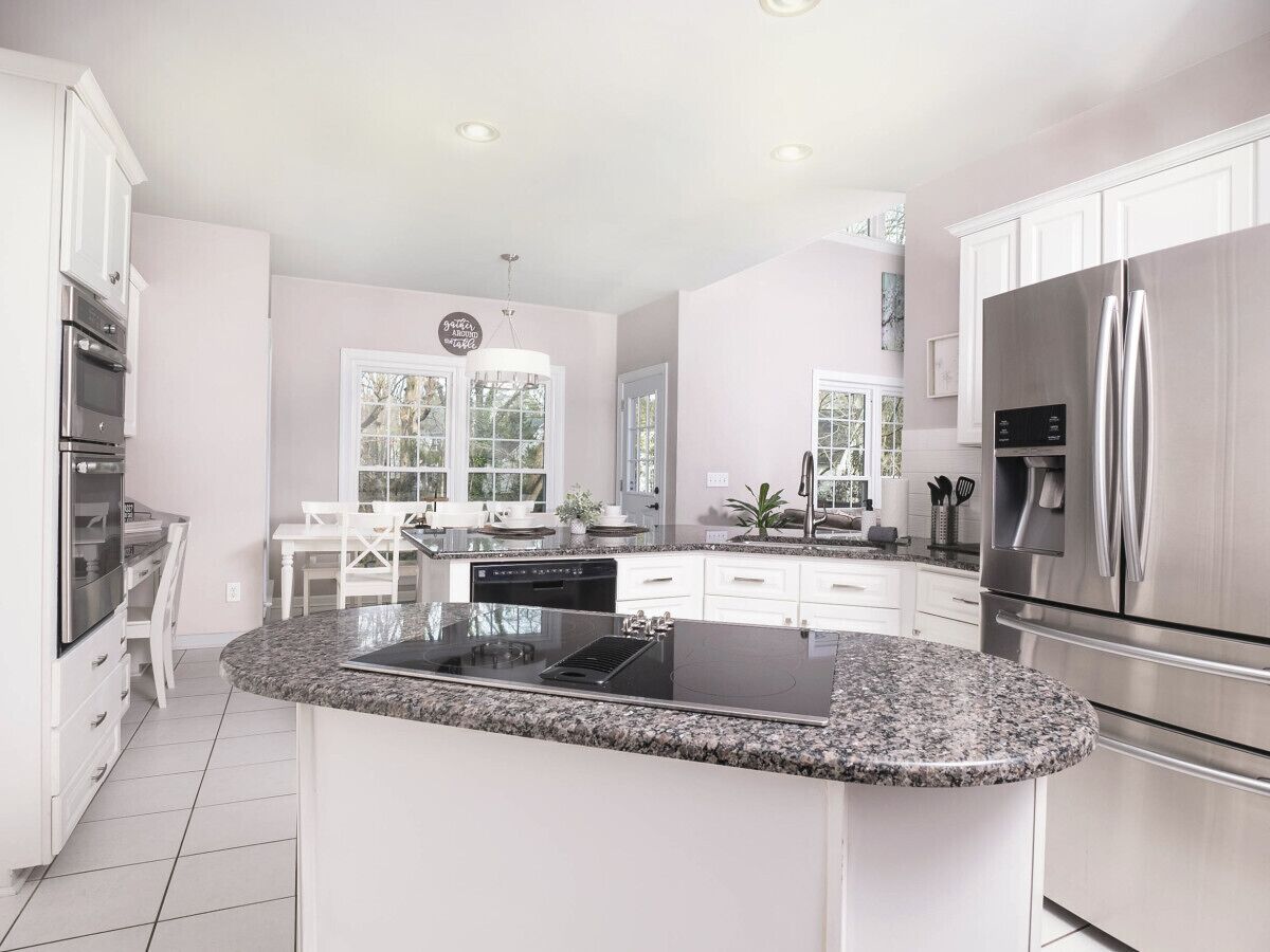 A modern kitchen with white cabinetry, stainless steel appliances, and a granite countertop island.