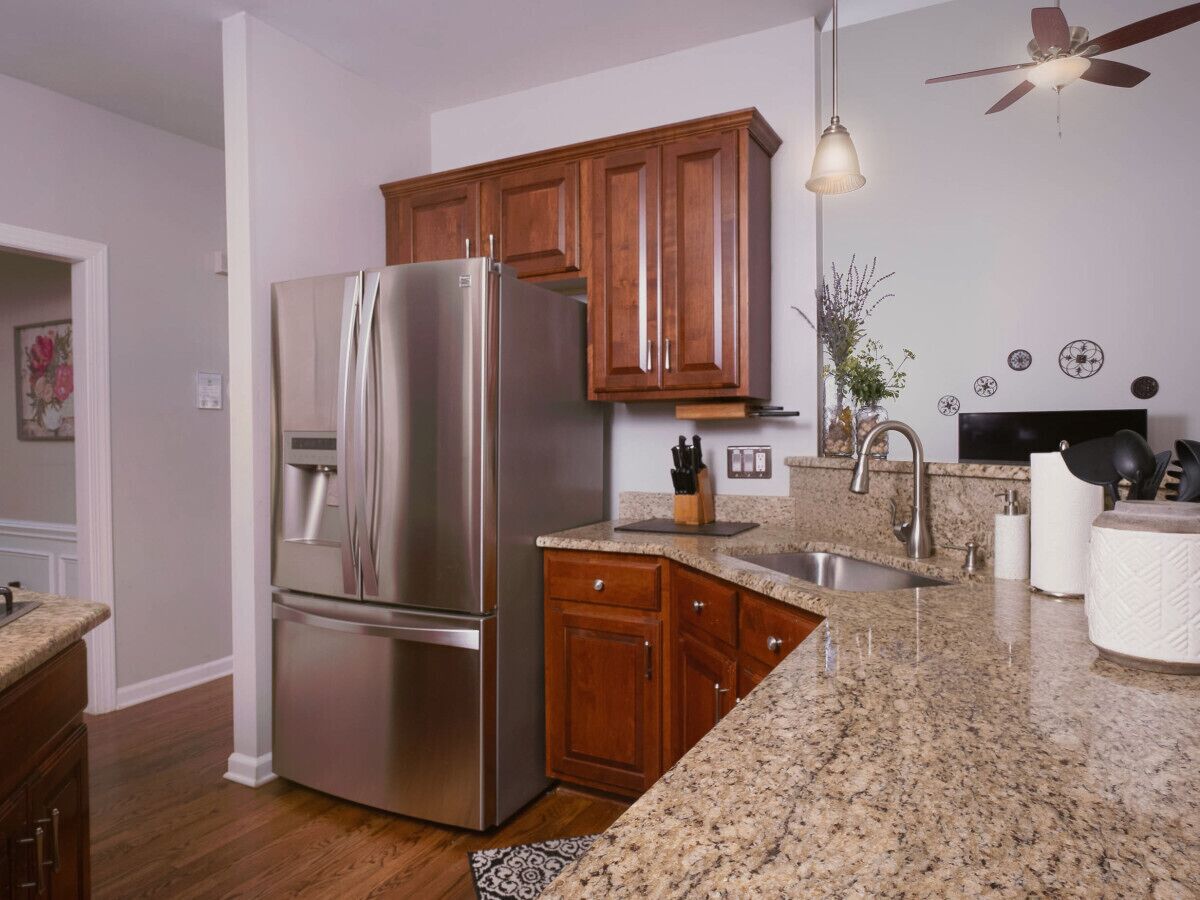 A kitchen with wooden cabinets, a stainless steel refrigerator, granite countertops, a sink, and a ceiling fan.