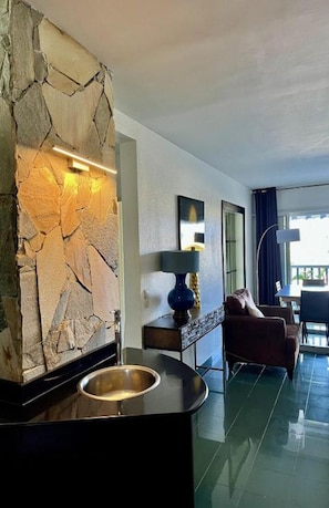 A modern hotel lobby with a stone accent wall, a round black sink, a dark lamp, a brown sofa, and a view of the outdoors. - Superb T3 luxuriously furnished marina Gosier (Le Gosier)
