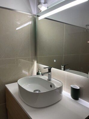Une salle de bain avec un lavabo blanc, un miroir et une tasse verte posée sur le comptoir.