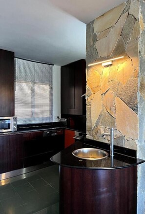 A modern kitchen with a stone accent wall, a built-in microwave, and a round island with a sink.