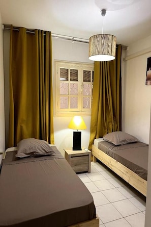 Une chambre avec deux lits, une fenêtre avec des rideaux, une lampe et un luminaire au plafond.